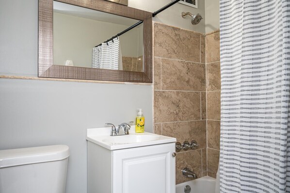 Une salle de bain avec un lavabo blanc, un miroir, une douche avec un rideau à rayures et des toilettes.