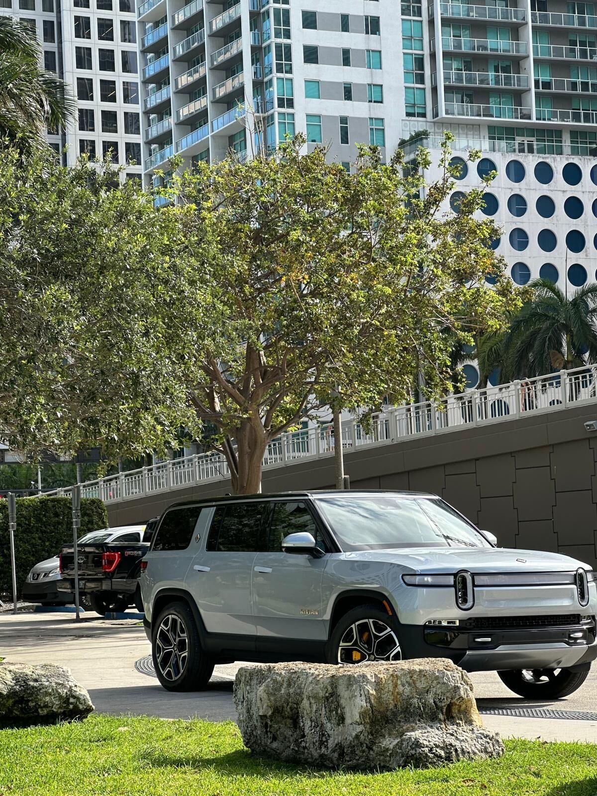 Ein modernes Gebäude mit einem einzigartigen, kreisförmigen Fensterdesign, eine von Bäumen gesäumte Straße und ein geparktes SUV.