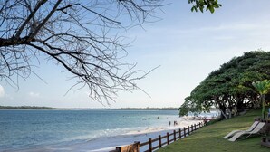 Una playa con un cerco de madera, un área verde con sillas de descanso y vistas al océano.