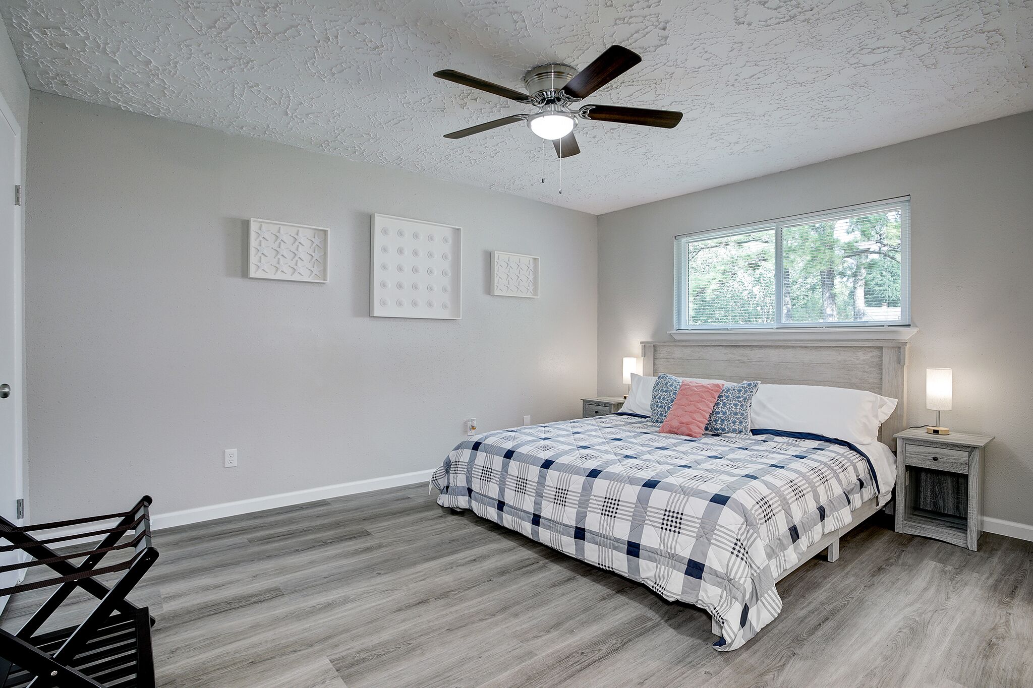 A bedroom with a bed, a ceiling fan, a window, and a nightstand with a lamp.