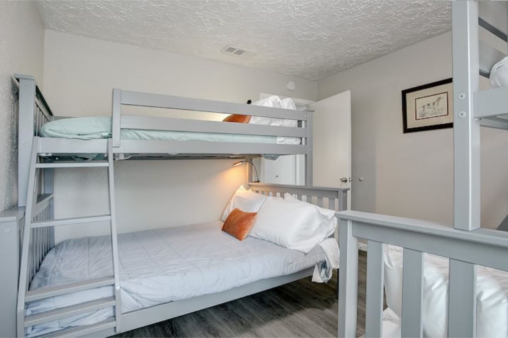 A bunk bed room with white bedding and a single orange pillow.