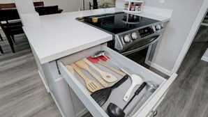 Une cuisine avec un plan de travail blanc, une cuisinière et un tiroir contenant des ustensiles de cuisine.