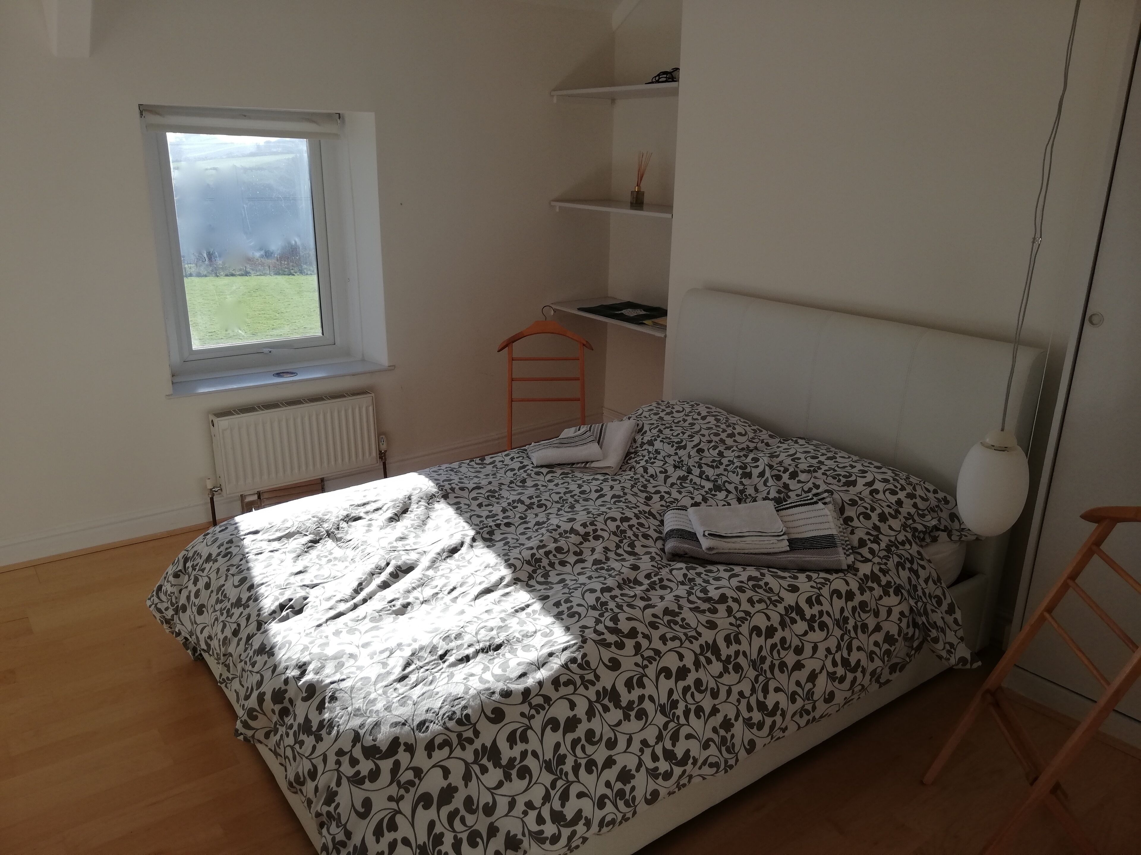 Une chambre à coucher avec un lit, une fenêtre, un radiateur, une étagère et une lampe suspendue.