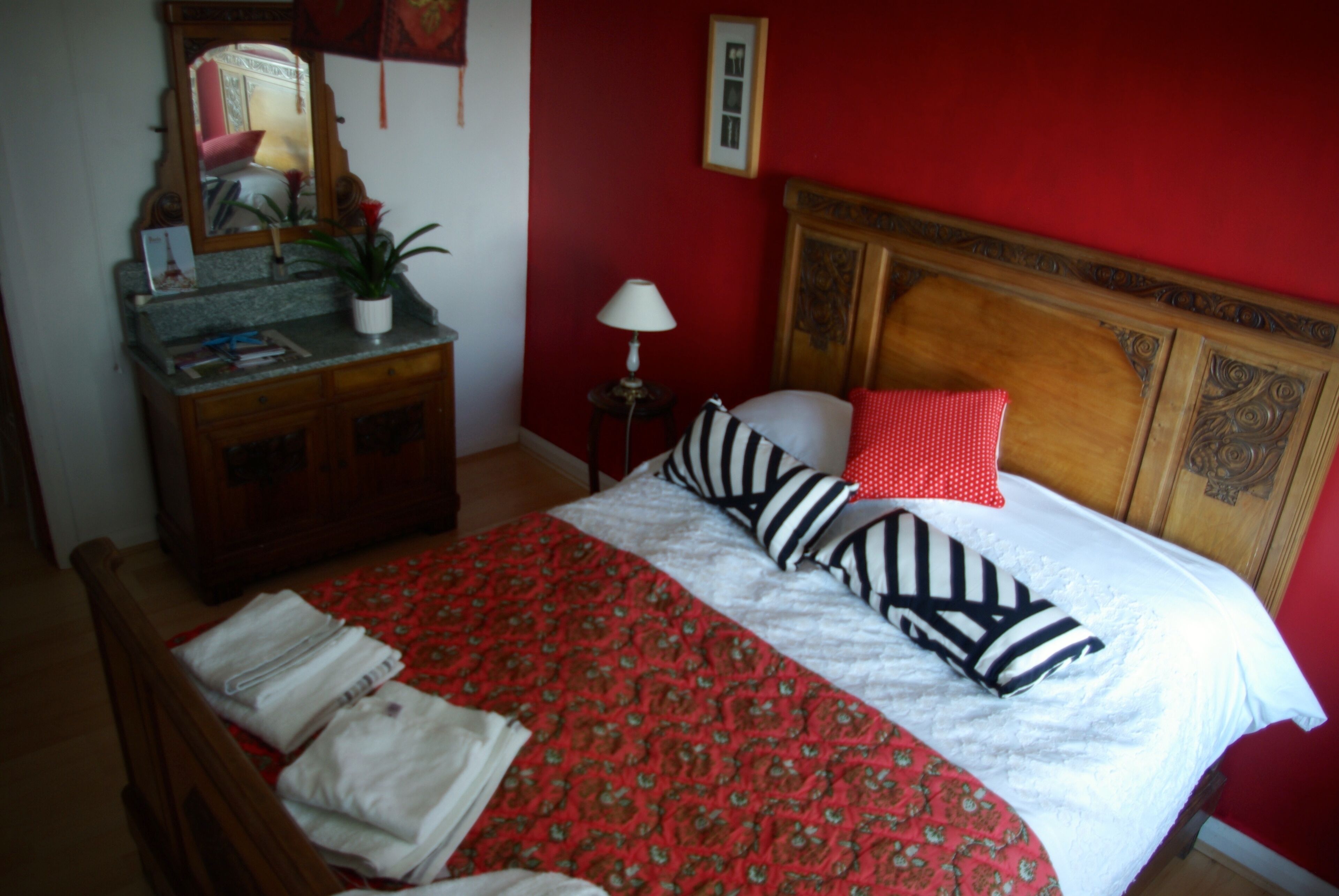 Una camera da letto con una testiera in legno, una parete rossa, un letto con copripiumino a motivi rossi e bianchi e un comodino con una lampada.
