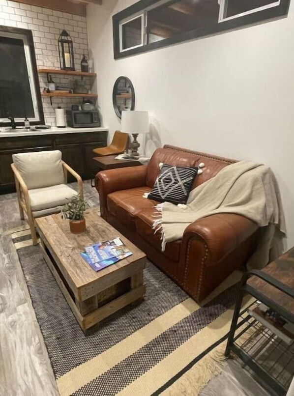 A cozy living room with a brown leather sofa, a wooden coffee table, and a beige armchair. A striped rug covers the floor, and a small plant is on the coffee table. - Peaceful new Tiny Home on farm, steps to wineries!
(Escondido)