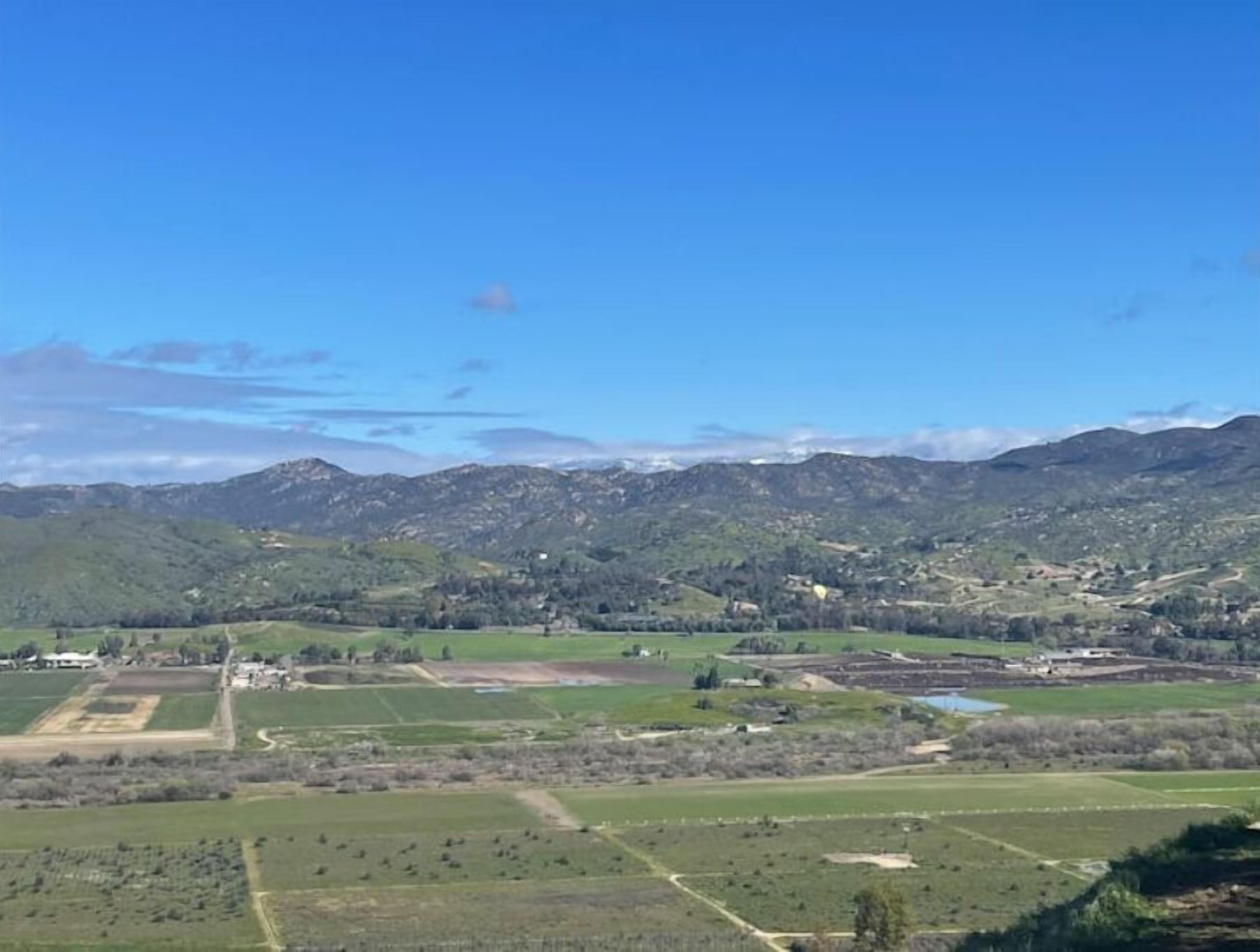A rural landscape with fields, a few buildings, and mountains in the background.