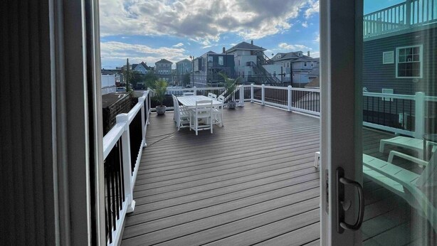 A wooden deck with a white railing, a table, and chairs, overlooking a residential area with houses and a clear sky. - Big Deck Energy-1 block to Beach & Boardwalk (Atlantic City)