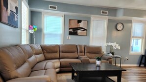 A living room with a brown leather sectional sofa, a dark wooden coffee table, and a beige rug. - Big Deck Energy-1 block to Beach & Boardwalk (Atlantic City)