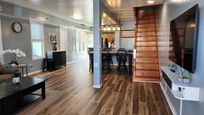 A spacious living area with a wooden floor, a dining area with chairs, a kitchen in the background, and a staircase leading to another level. - Big Deck Energy-1 block to Beach & Boardwalk (Atlantic City)