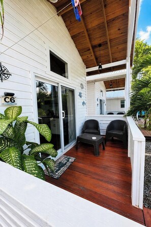 A covered porch with a wooden ceiling, a sliding glass door, and two wicker chairs.