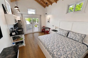 A bedroom with a bed, a desk, a chair, a table, and a balcony with a view.