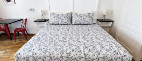 A bed with a floral bedspread, a white headboard, and two bedside tables with lamps.