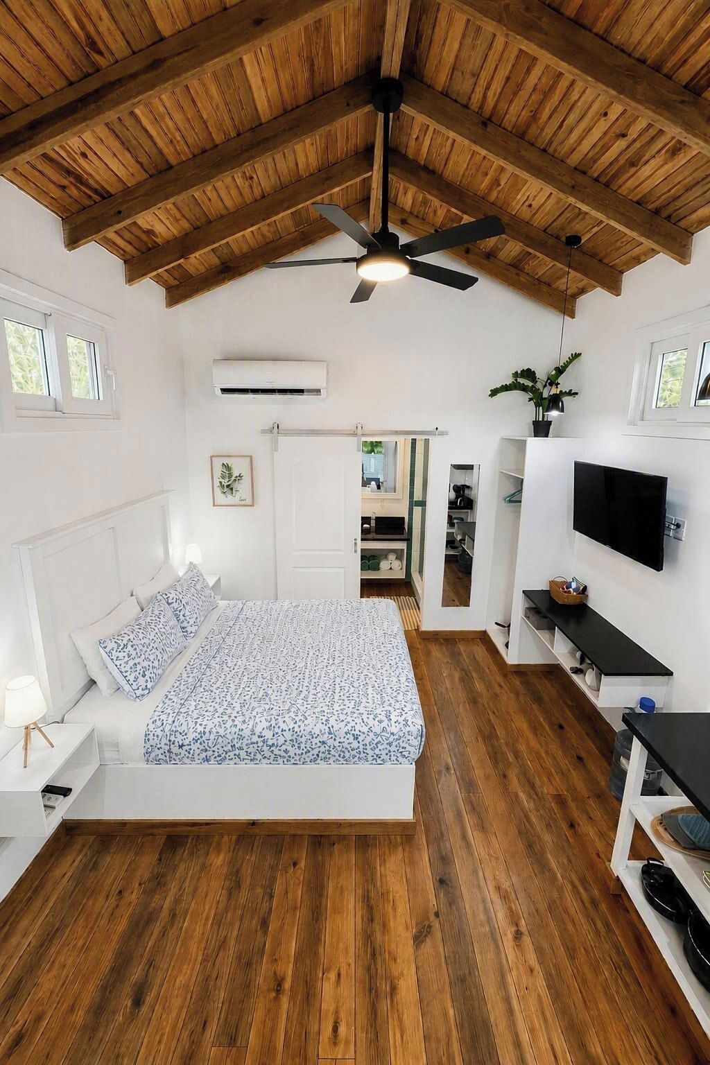 Een slaapkamer met een bed, een plafondventilator, een televisie en een plant.