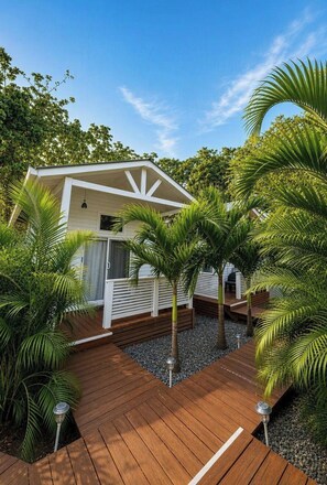 A white building with a wooden deck, surrounded by palm trees and a clear sky. - Brand New Fully Equipped Island Cabin (West Bay, Roatán)