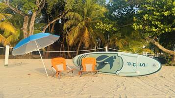 Uma praia com uma prancha de surf, duas cadeiras de praia e um guarda-sol.