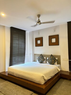 Un dormitorio moderno con una cama grande, un ventilador de techo y dos cuadros en la pared.