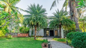 A well-maintained garden with a stone pathway leading to a building with a sign reading "VAGUNA". - Truliv Villa LAGUNA (Tirupporur)