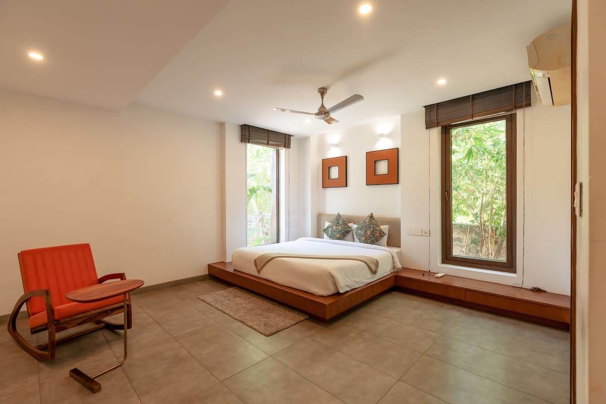 A bedroom with a bed, a chair, and large windows.