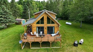 A log cabin with a deck, outdoor seating, and a water tank in a forested area.