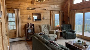 A cozy cabin interior with a large window, a chandelier, and a fireplace. - Log Cabin on 6 acres w direct ATV trail access, firepit, mountain views ,sunsets (Colebrook)