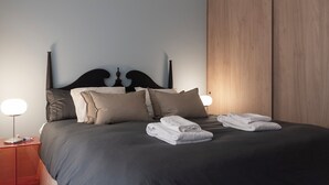 Un lit bien fait, avec des oreillers et des serviettes pliées, une table de chevet avec une lampe et une armoire en bois dans une chambre d’hôtel.