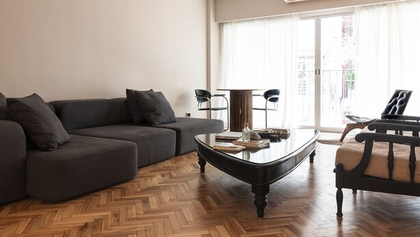 Un salon moderne avec un canapé gris foncé, une table basse en bois sur laquelle sont posés des livres et un fauteuil noir.