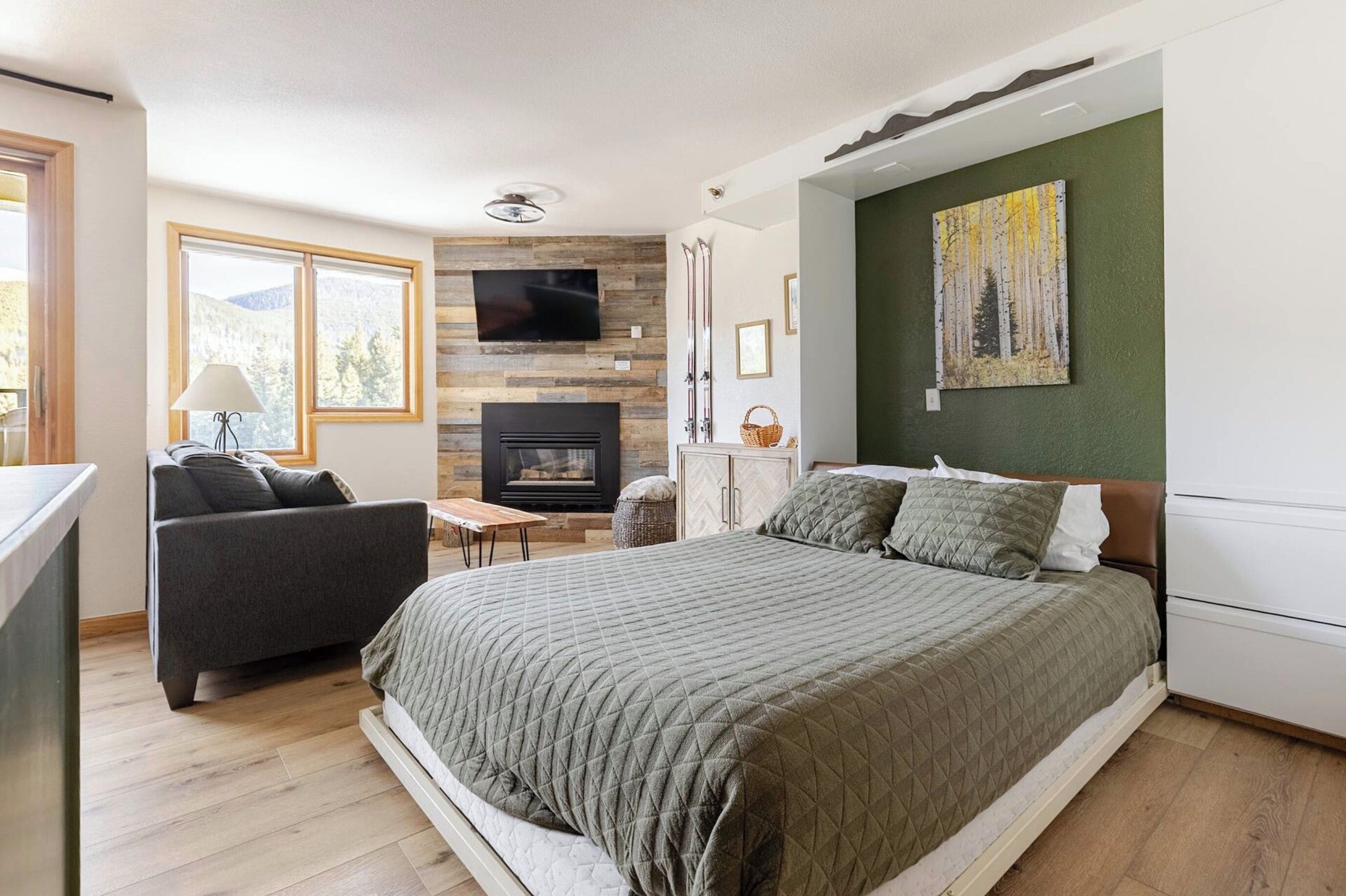 A modern bedroom with a large bed, a TV mounted on the wall, a fireplace, and a painting on the wall.