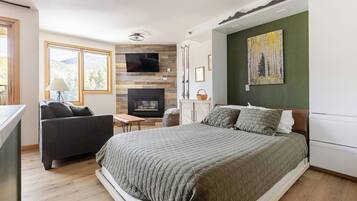 A modern bedroom with a large bed, a TV mounted on the wall, a fireplace, and a painting on the wall.