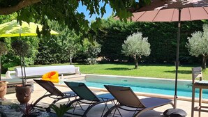 Area piscina con lettini, una pergola e un giardino curato con ciottoli e piante.