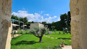 Una vista attraverso un arco in pietra di un giardino curato, con un albero centrale, un vialetto in pietra e un edificio in pietra sullo sfondo.