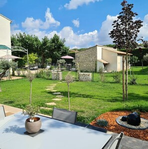 Un espace patio aménagé avec une table et des chaises, entouré d’une pelouse bien entretenue et d’un mur en pierre.