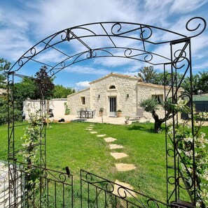 Une maison en pierre avec un jardin et un portail en métal.