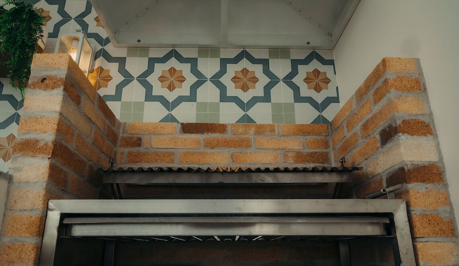 Un four en briques avec une porte en métal, entouré de carreaux décoratifs et agrémenté d’une plante.