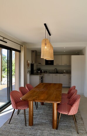 Een moderne keuken met witte kasten, een houten eettafel en rode, geruite stoelen.
