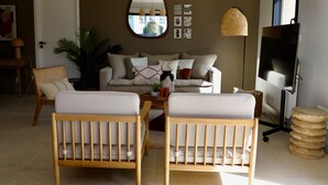 A living room with a sofa, two wooden chairs, a coffee table, a lamp, a TV, and a mirror on the wall. - Maison Décorée Avec Charme, Parfaitement Équipée Pour 6 Personne, Proche Plage (Barneville-Carteret)