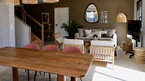 A modern living room with a wooden dining table, a sofa set, and a TV. - Maison Décorée Avec Charme, Parfaitement Équipée Pour 6 Personne, Proche Plage (Barneville-Carteret)