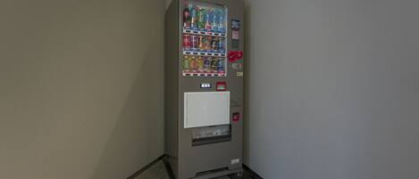 Máquina expendedora con diversas bebidas y aperitivos, una ranura para pagos y una ranura para devolución de monedas.