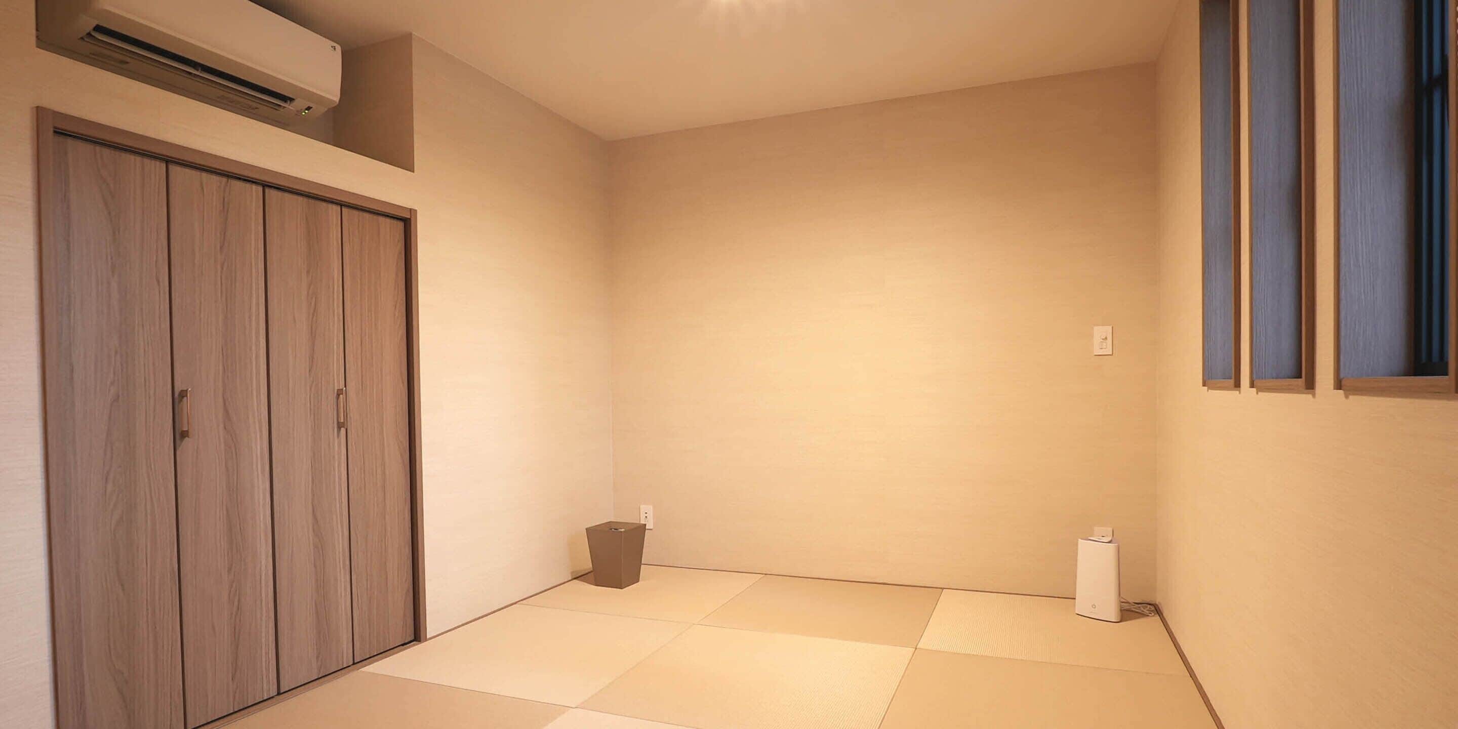 Une pièce avec un sol recouvert de tatamis, une armoire en bois, une petite poubelle et un purificateur d’air blanc.