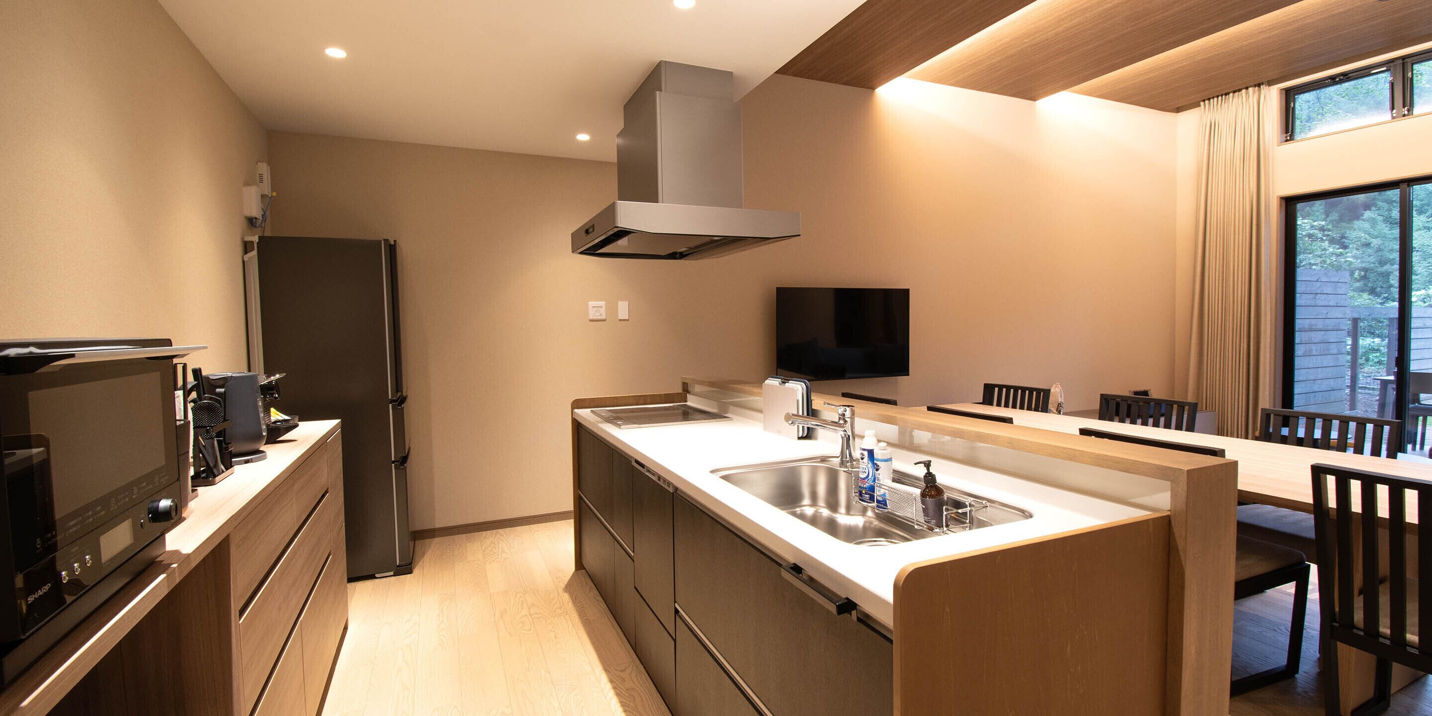 A modern kitchen with a built-in stove, a large sink, and a dining area with wooden chairs and a table.