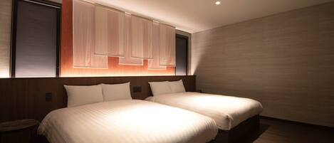 Une chambre d’hôtel moderne avec deux lits, une tête de lit en bois et une grande fenêtre avec des stores.