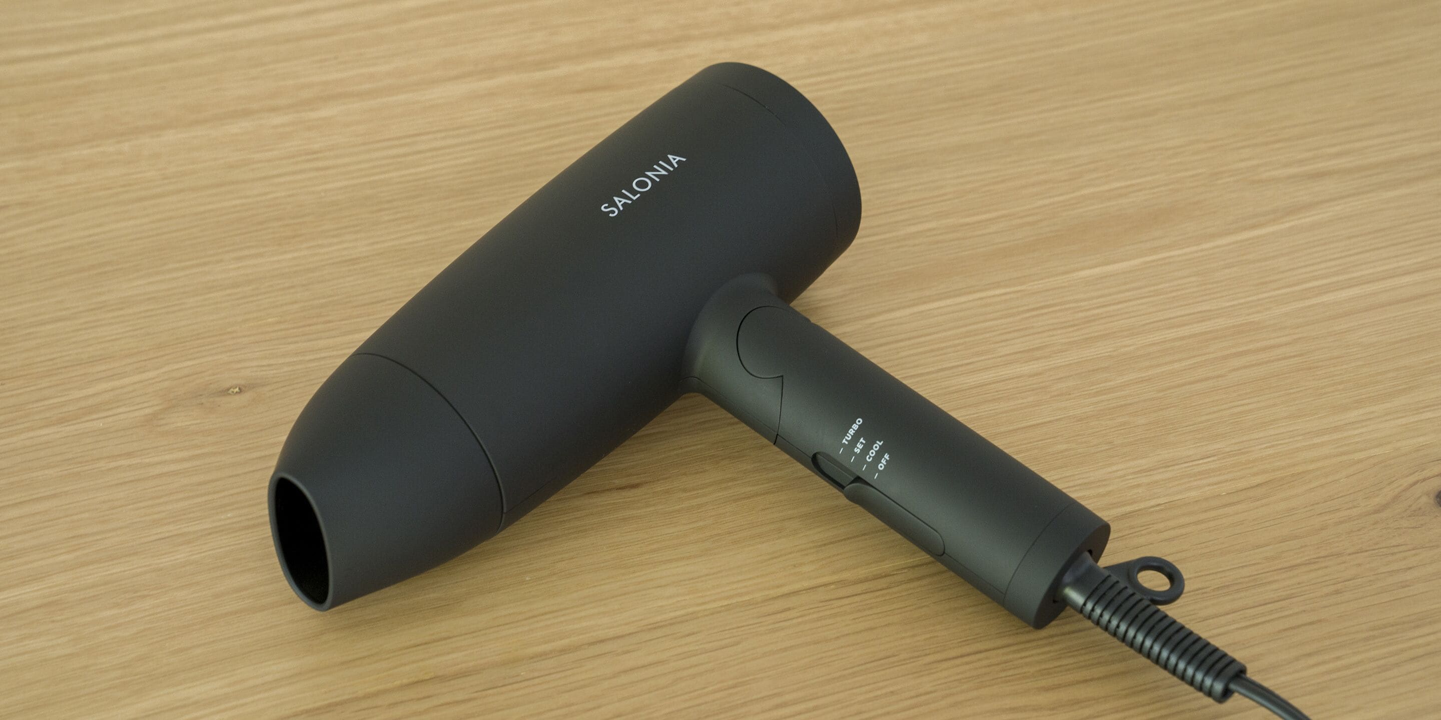 A black hairdryer with a cord on a wooden surface.