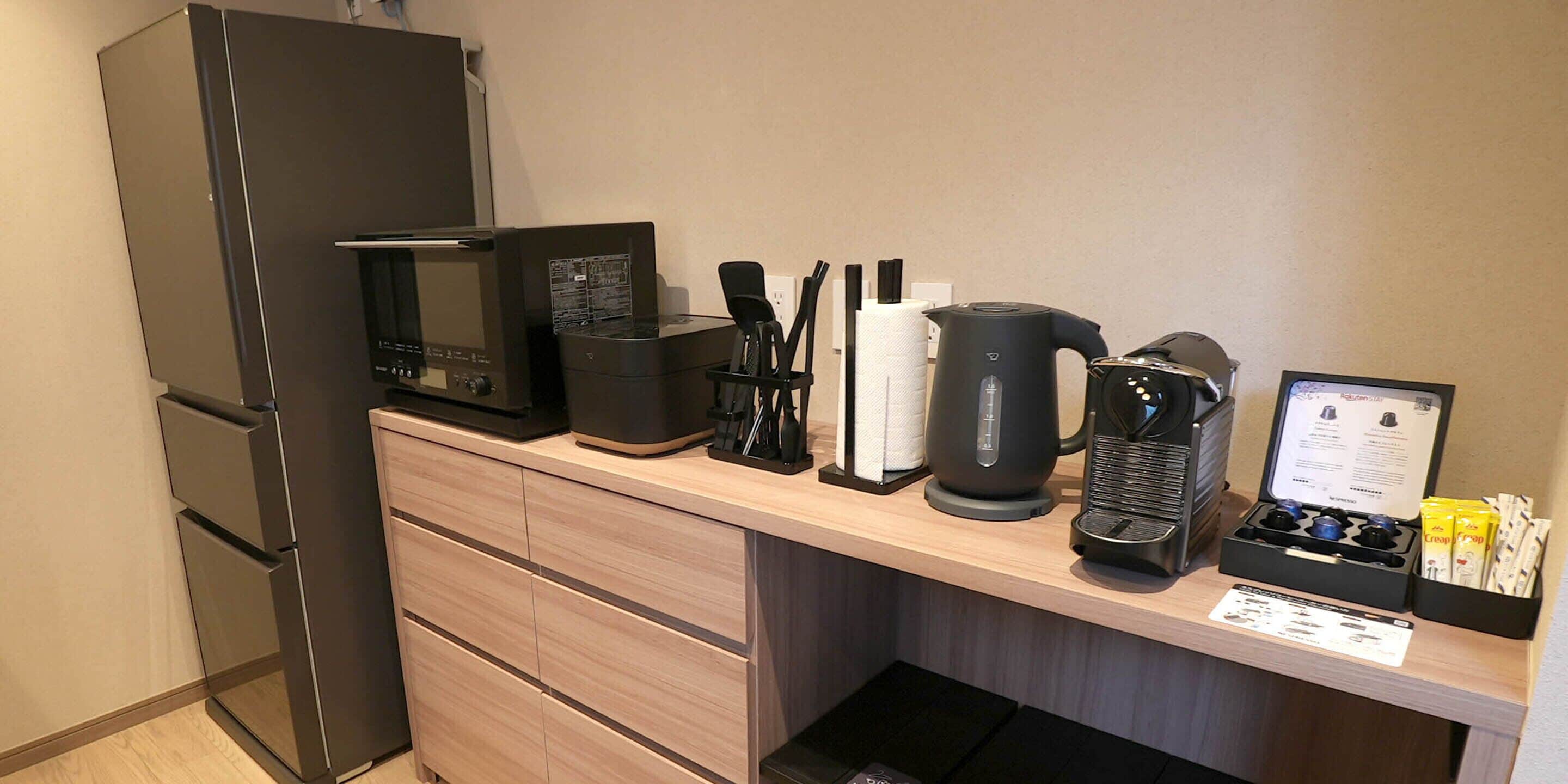 A kitchenette with a microwave, coffee maker, kettle, and tea set.