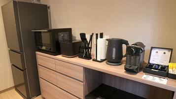 A kitchenette with a microwave, coffee maker, kettle, and tea set.