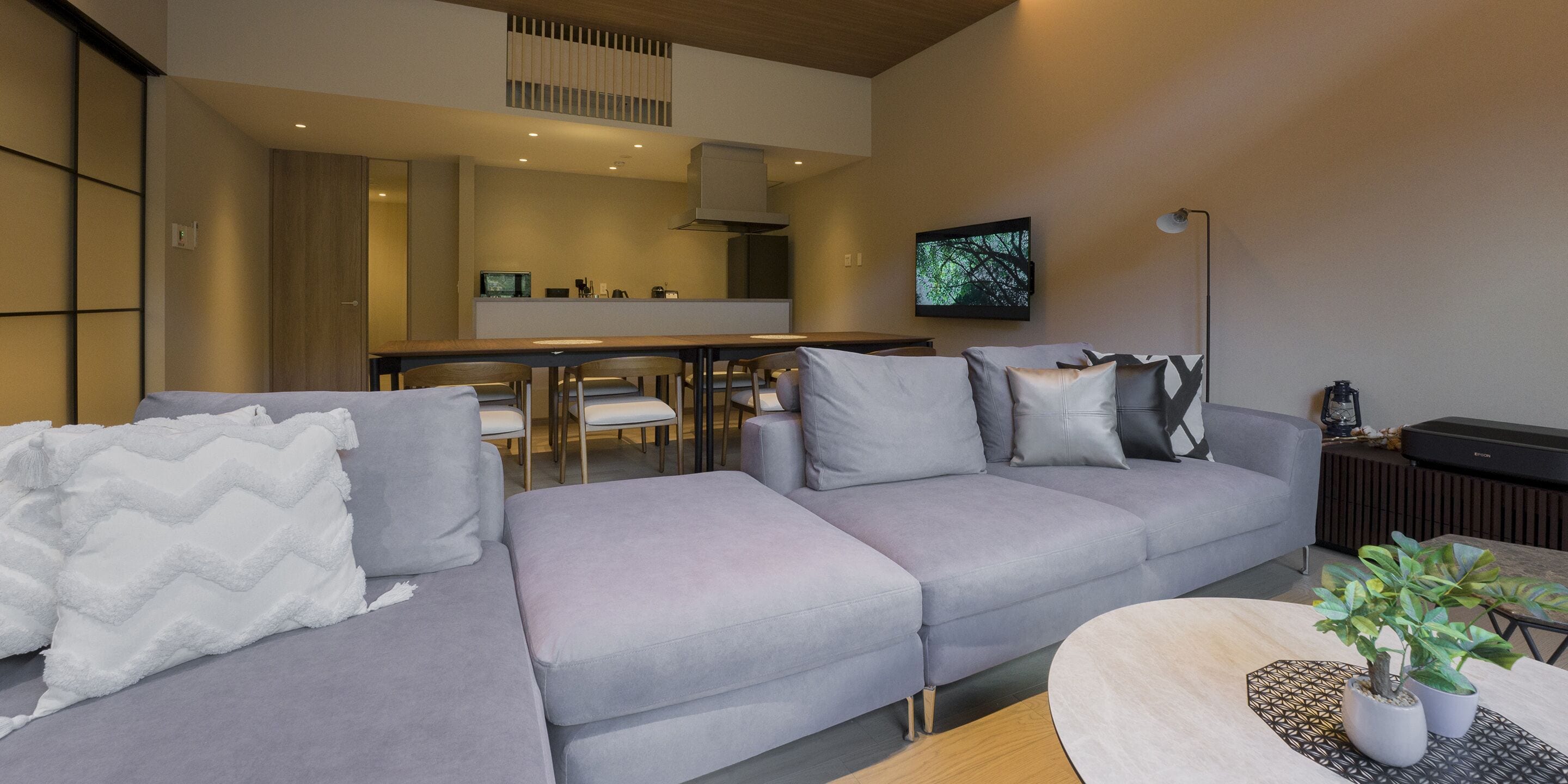 Un salon moderne avec un canapé gris, une table basse et un téléviseur fixé au mur.