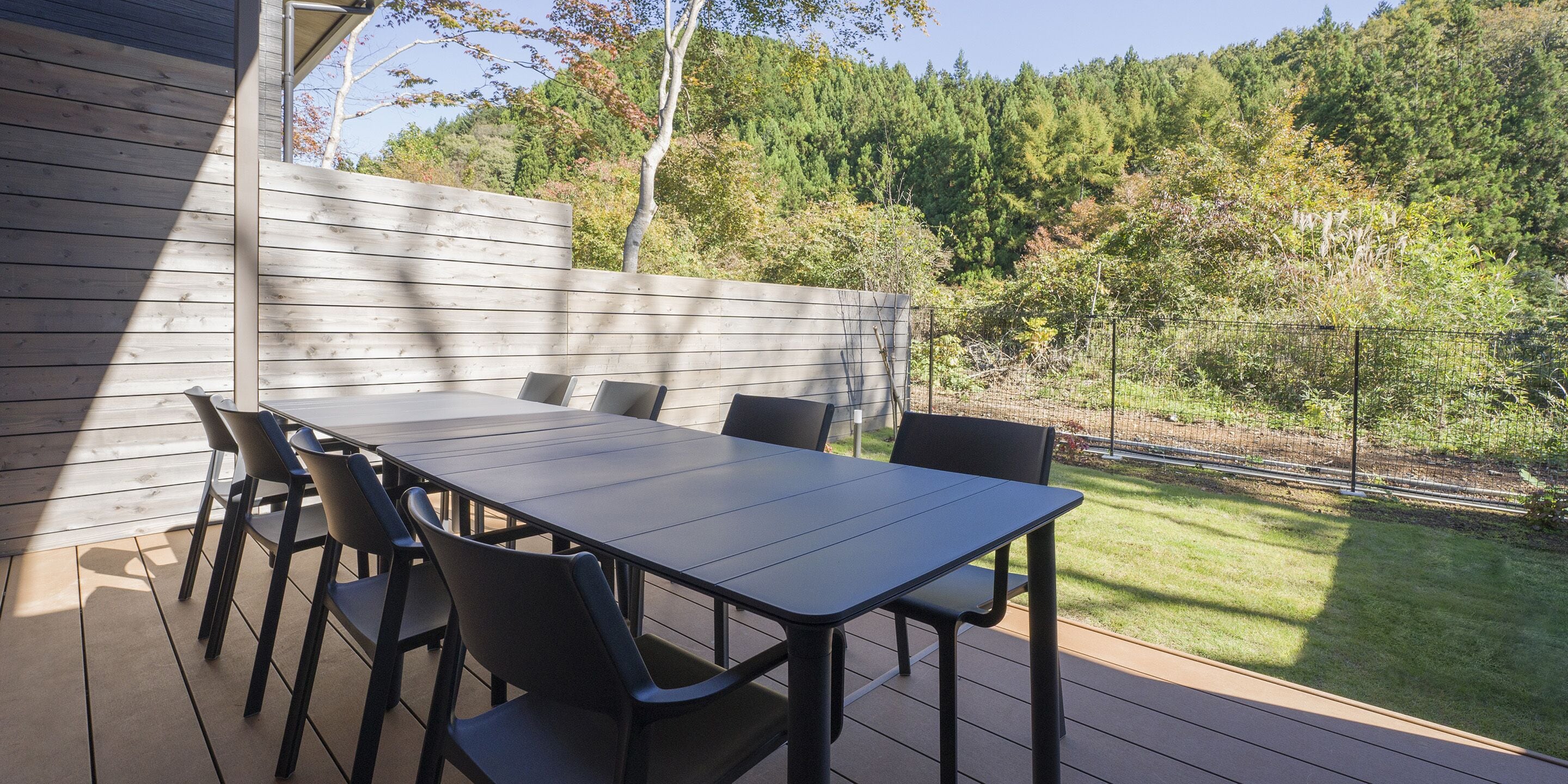 An outdoor patio with a wooden deck, a table, and chairs.
