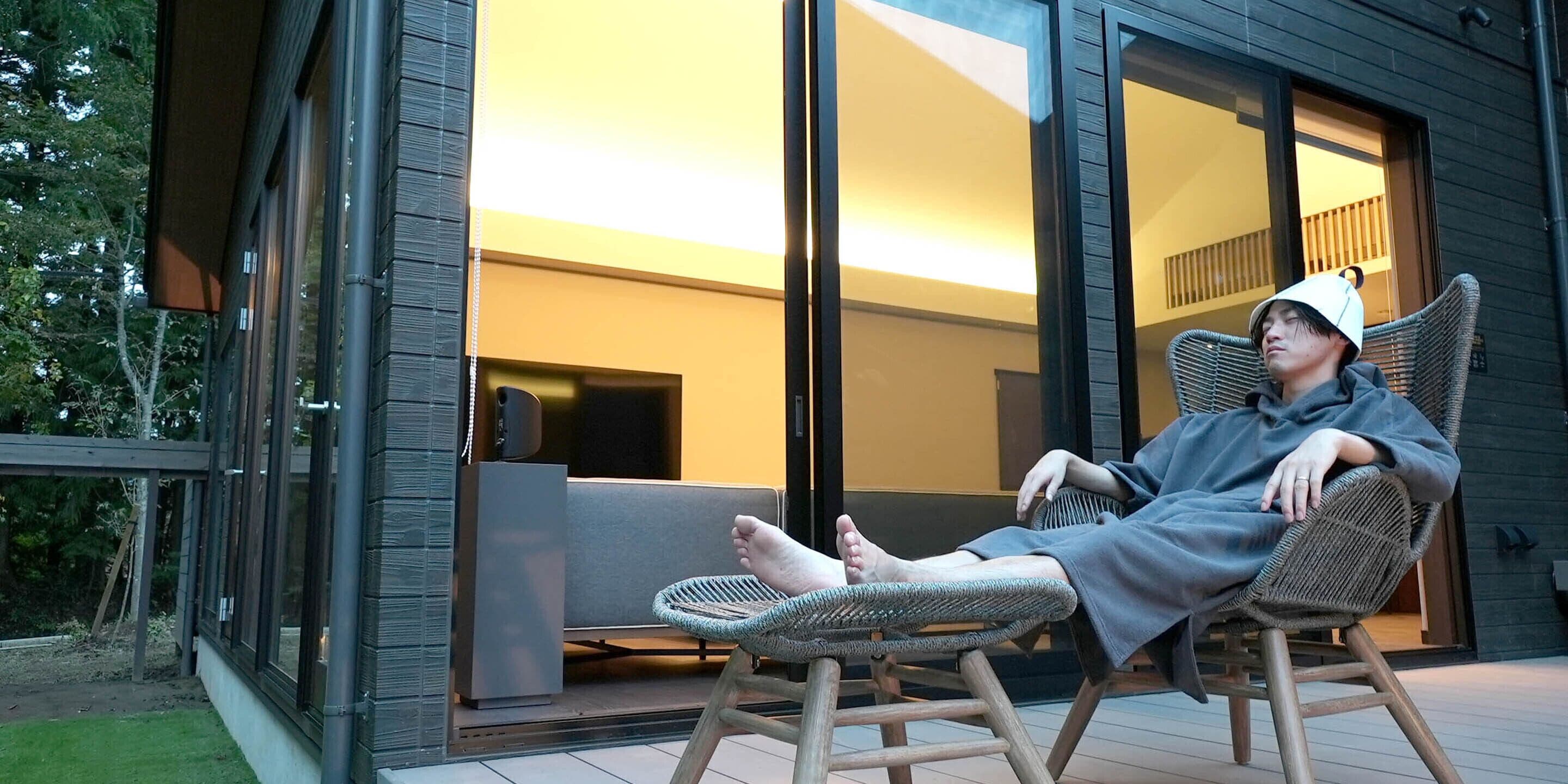 A person sitting on a wicker chair outside a modern building with large glass doors.