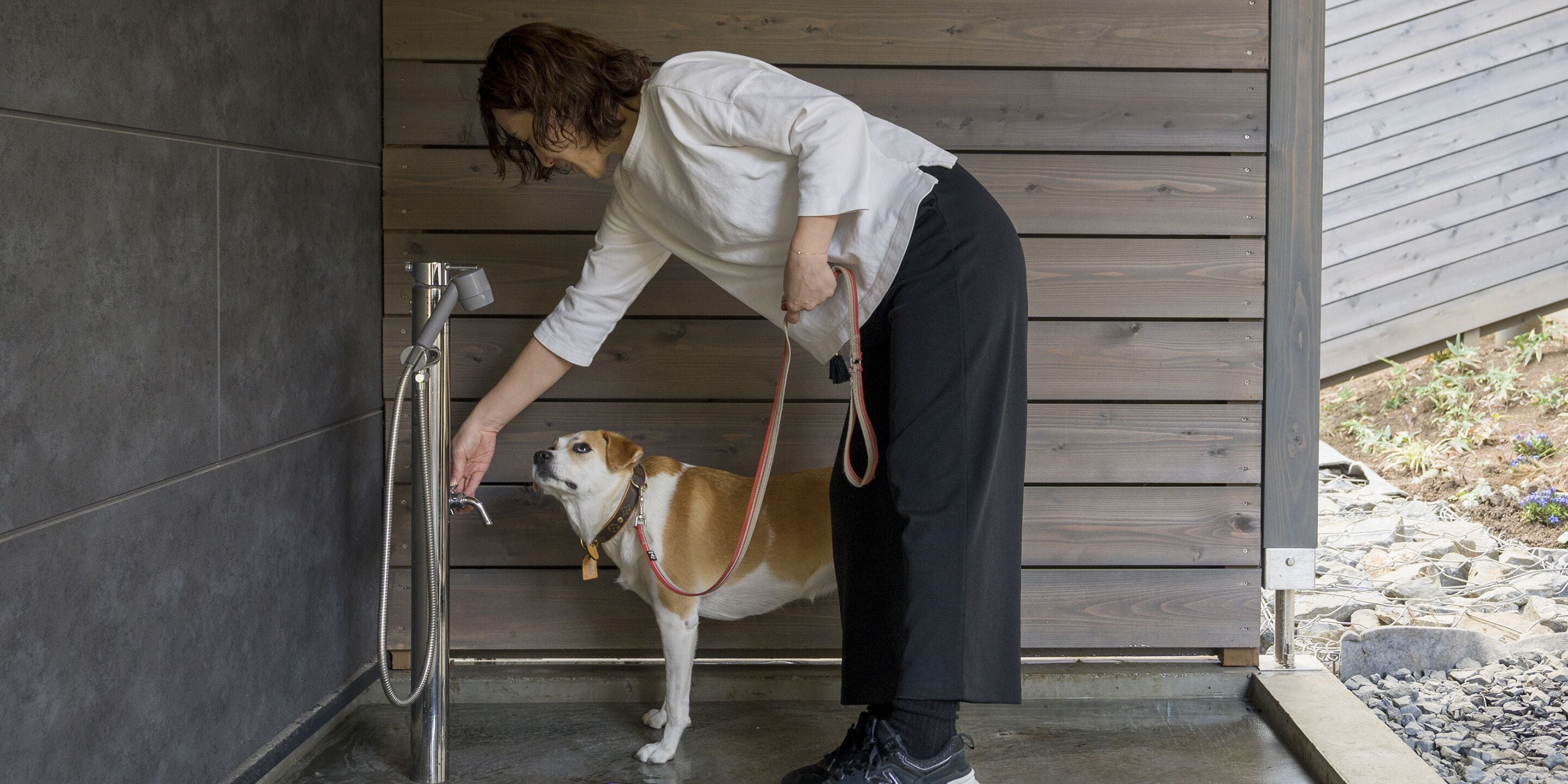 A person washing a dog in a shower area with wooden walls and a tiled floor.