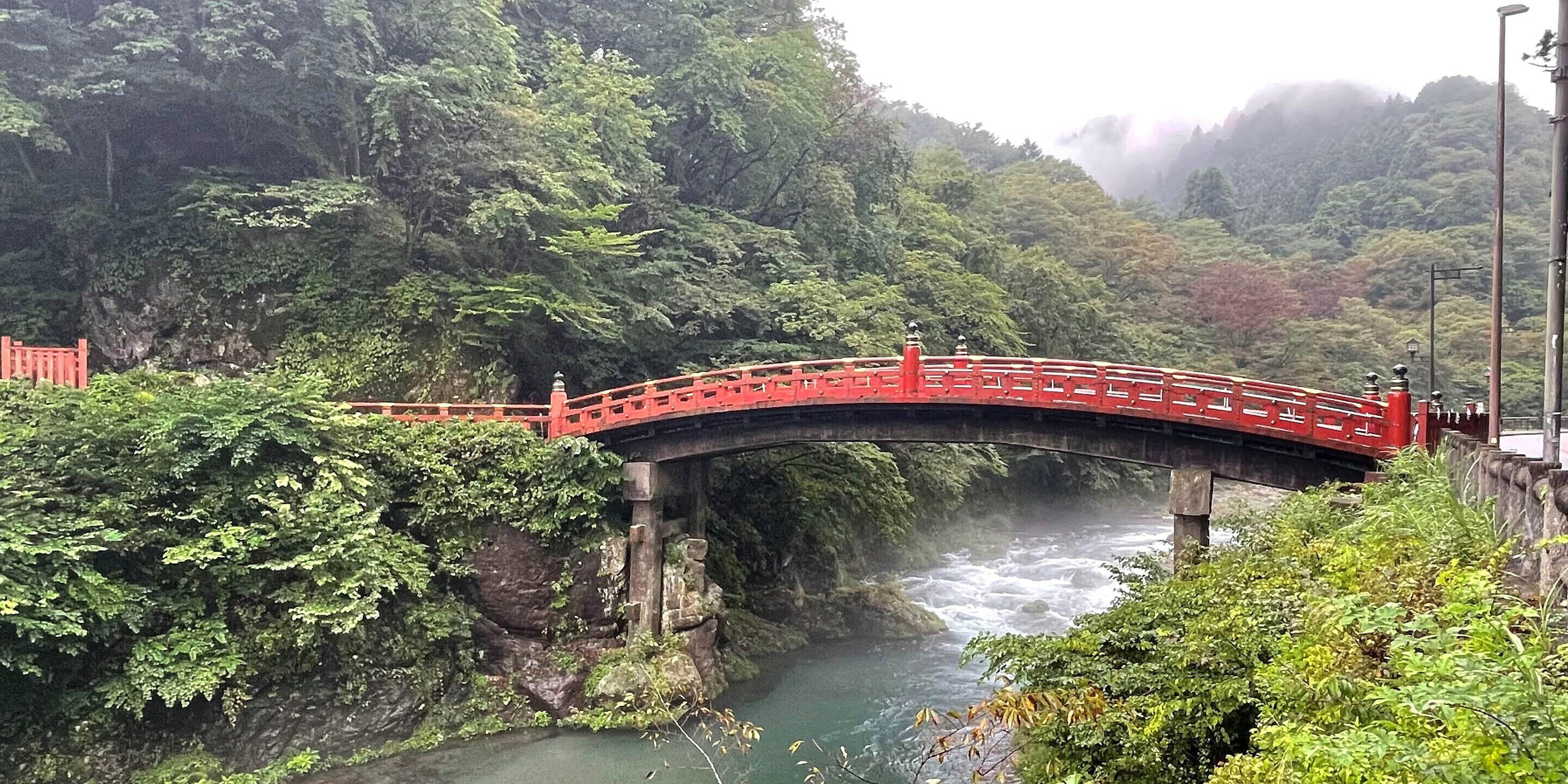 Un puente rojo sobre un río rodeado de exuberante vegetación.