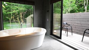 A modern bathroom with a freestanding bathtub, large windows, and a view of a wooden deck and greenery.