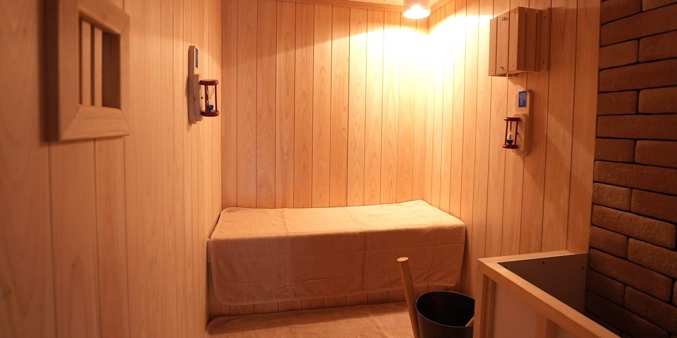 A wooden sauna room with a bench, a bucket, and a small wooden cabinet.